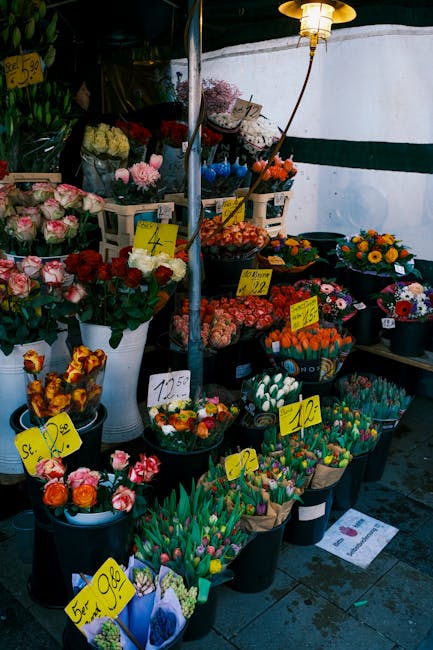 A display of fresh flower arrangements at Chadwell Heath flower shop, featuring bouquets of pink roses, red roses, and mixed seasonal flowers in black buckets and white vases. The flowers are arranged