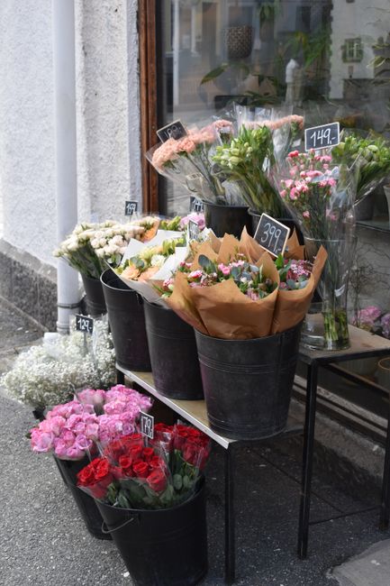 An outdoor display of floral bouquets arranged in black plastic buckets set on a metal table outside Chadwell Heath Flowers, a local florist. The arrangements feature a variety of fresh flowers in sof